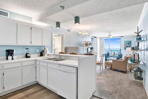 A modern kitchen with white cabinetry, a dishwasher, and a dining area with a view of the ocean. - Shoalwater 903 (Orange Beach)