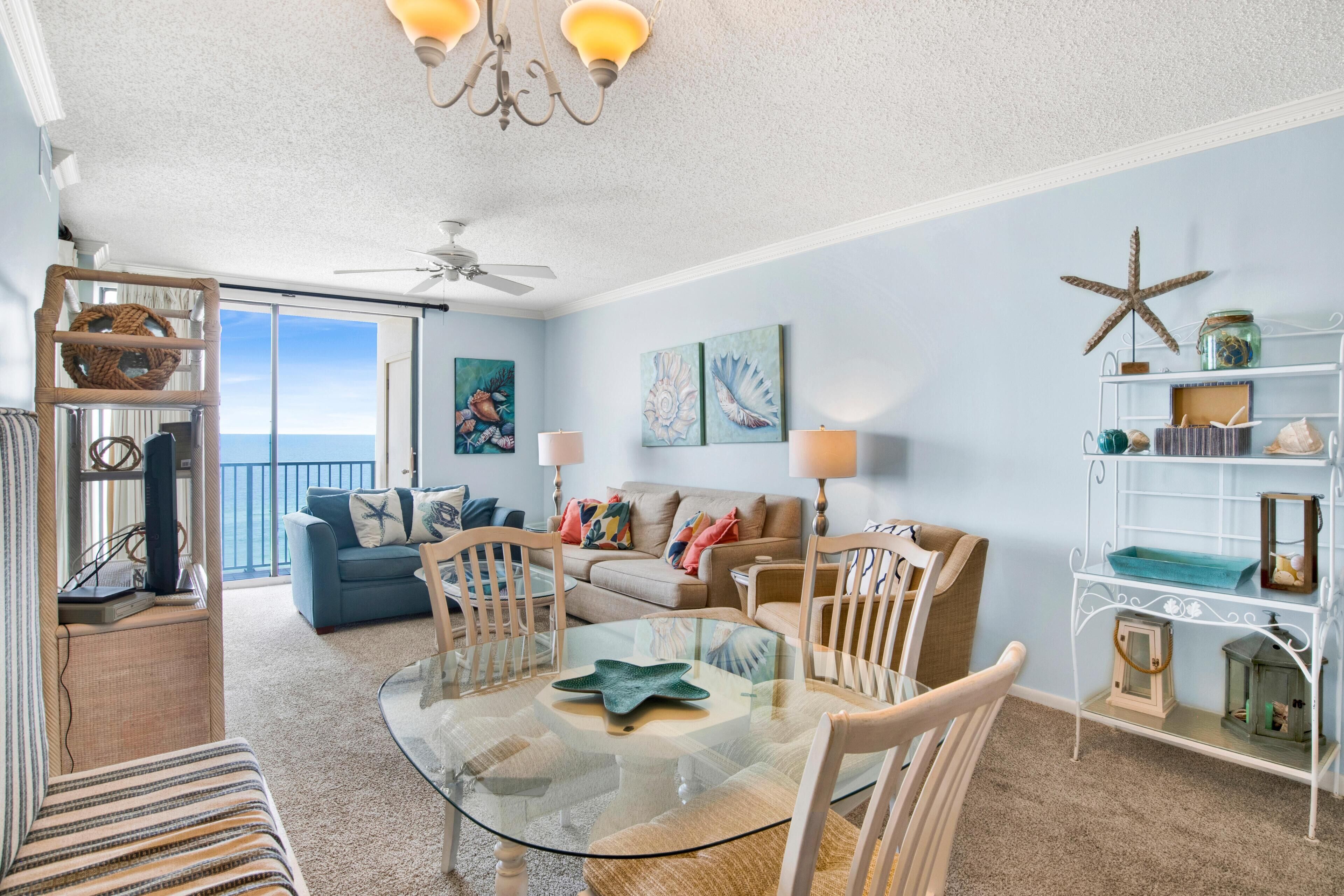 A living room with a glass table, two chairs, a sofa, and a balcony with a view.
