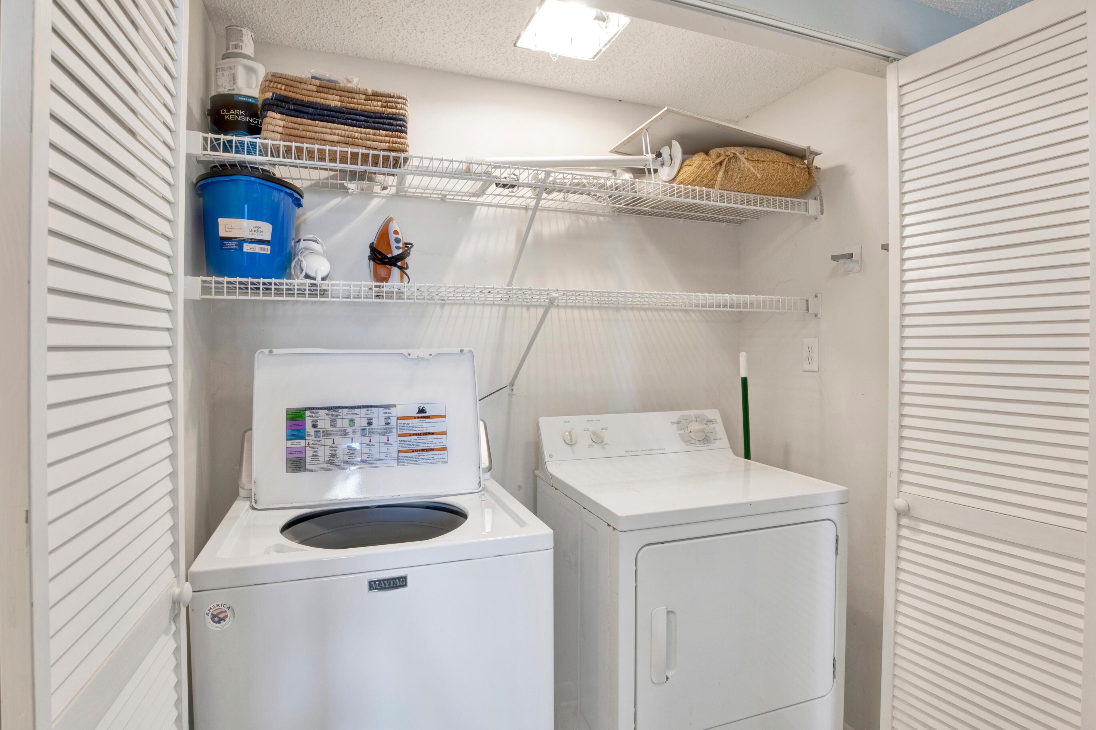 Une buanderie équipée d’un lave-linge et d’un sèche-linge à chargement frontal, d’étagères pour ranger les produits de lessive et d’un étendoir.