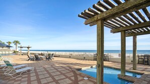 Un espace piscine doté de chaises longues et d’une pergola offrant une vue sur la plage.