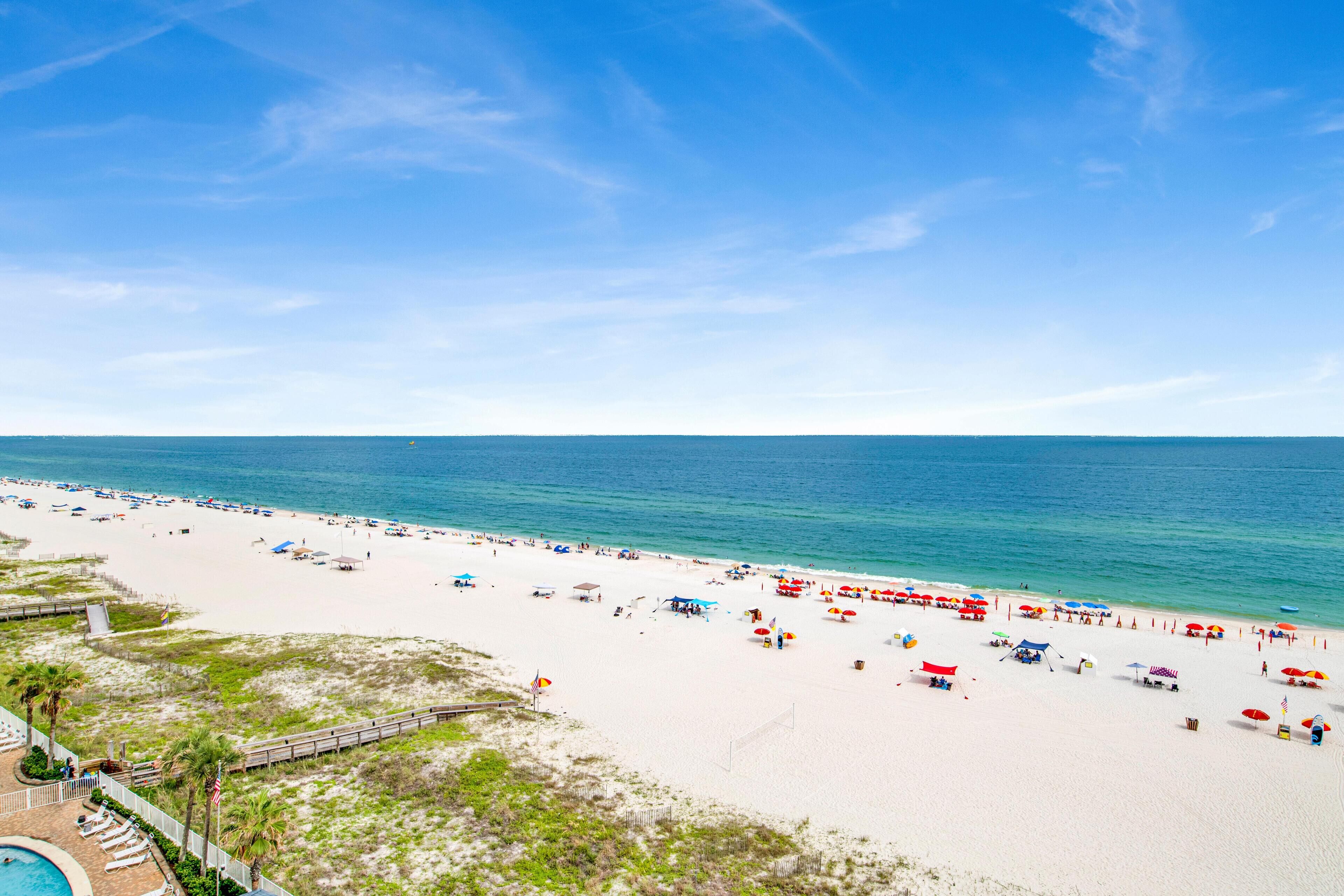 Ein Strand mit Poolbereich, Sonnenschirmen und blauem Himmel.