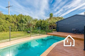 Relax by the pool surrounded by lush greenery and a wooden deck.