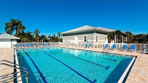 A swimming pool with clear blue water, surrounded by lounge chairs and a building with a white roof.