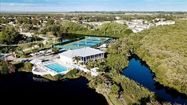 An aerial view of a resort with a large swimming pool, multiple buildings, and surrounding natural vegetation.