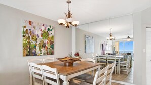A dining area with a wooden table and white chairs, a chandelier, and abstract art on the walls. - Windward Pointe 1002 (Orange Beach)