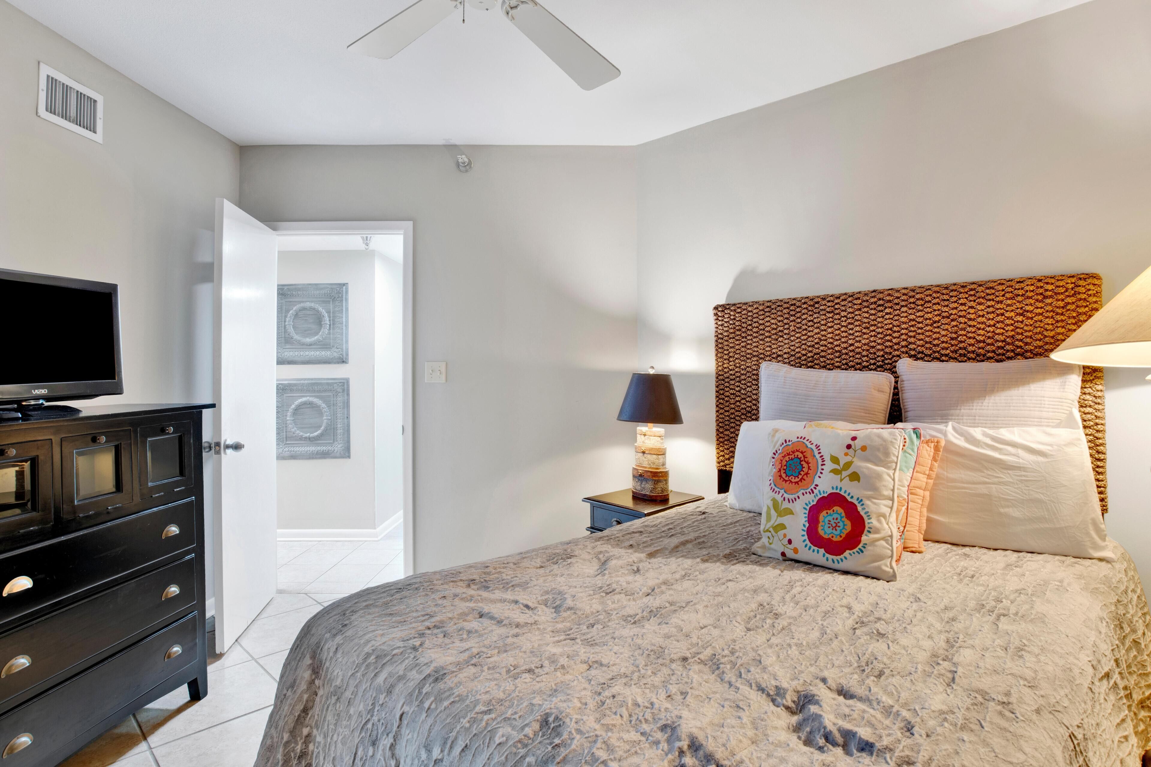 A bedroom with a bed, a dresser, a TV, a lamp, and a door.
