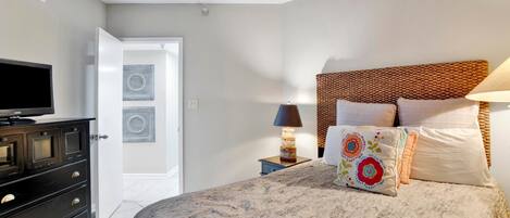 A bedroom with a bed, a dresser, a TV, a lamp, and a door.