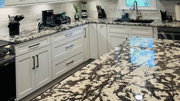 Cozinha moderna com armários brancos, bancadas de granito e lustres de cristal.
