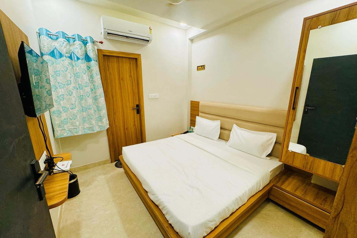 Une chambre d’hôtel comprenant un lit, une armoire en bois, un miroir, un appareil de climatisation, une porte et un rideau.