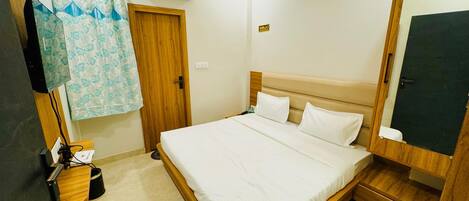 A hotel room with a bed, a wooden wardrobe, a mirror, an air conditioning unit, a door, and a curtain.