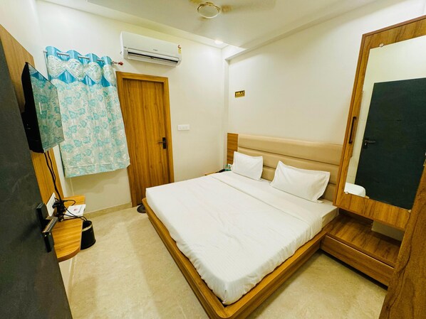 A hotel room with a bed, a wooden wardrobe, a mirror, an air conditioning unit, a door, and a curtain. - Hotel Najaf Palace 200 Mtrs from Dargah (Ajmer)