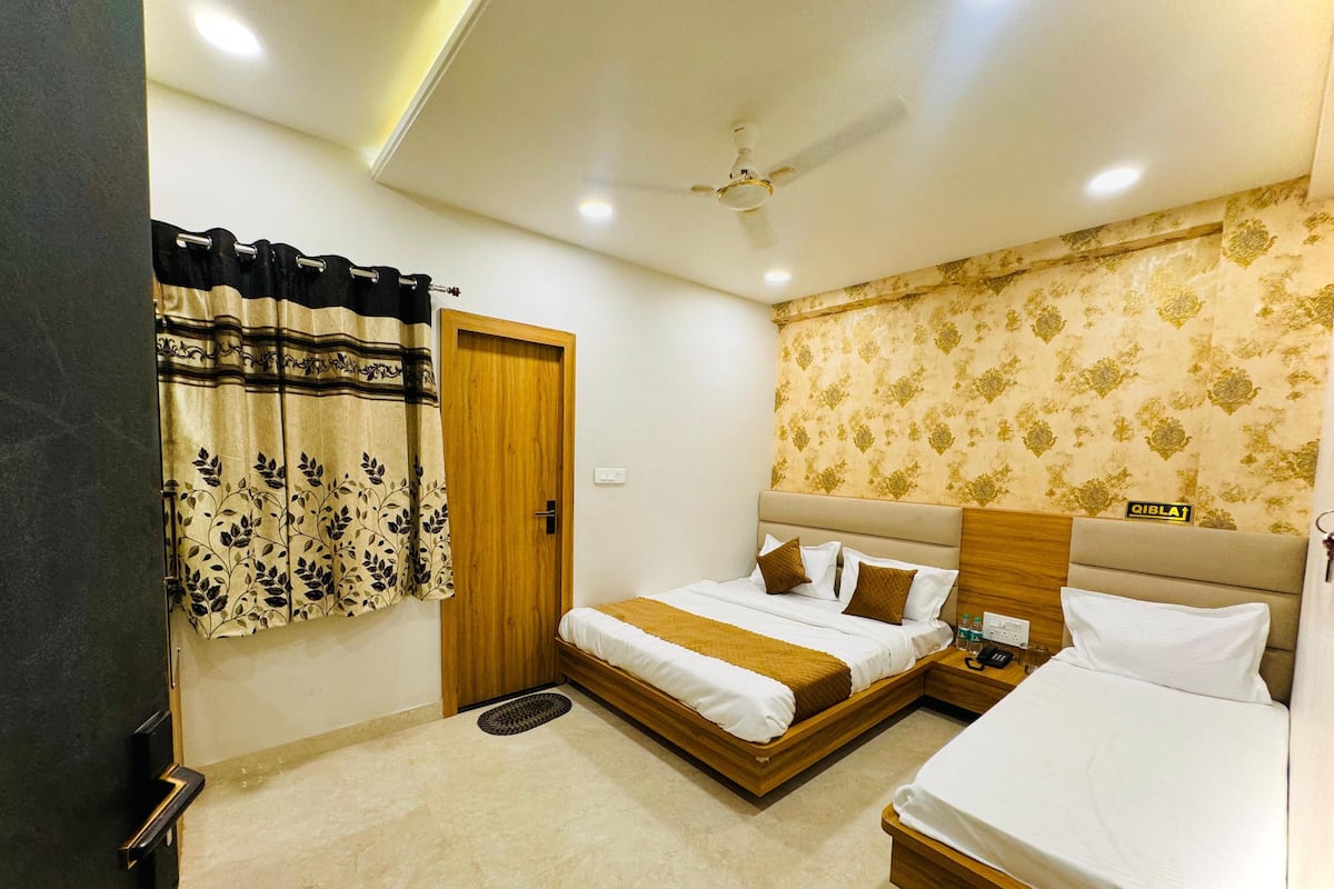 Une chambre d’hôtel avec deux lits, une tête de lit en bois, un ventilateur de plafond et un papier peint à motifs.