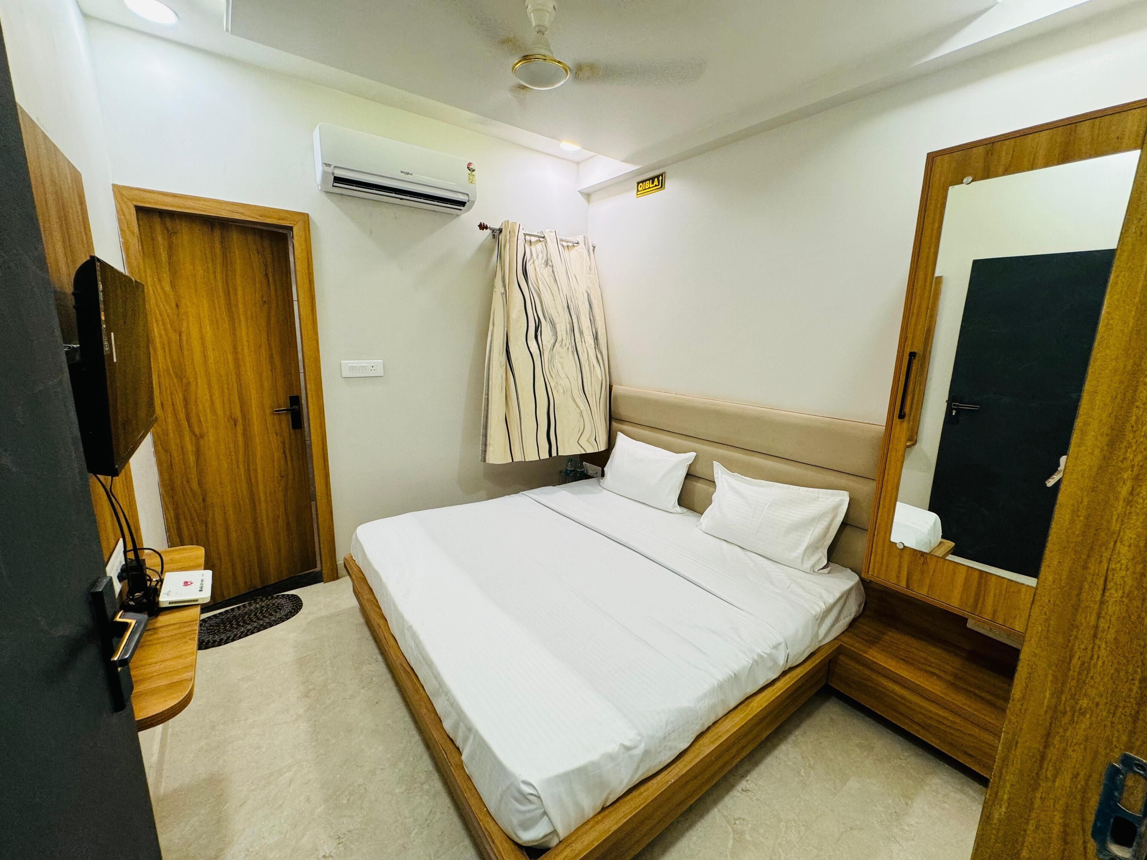 A bedroom with a bed, a TV, an air conditioner, and a mirror.