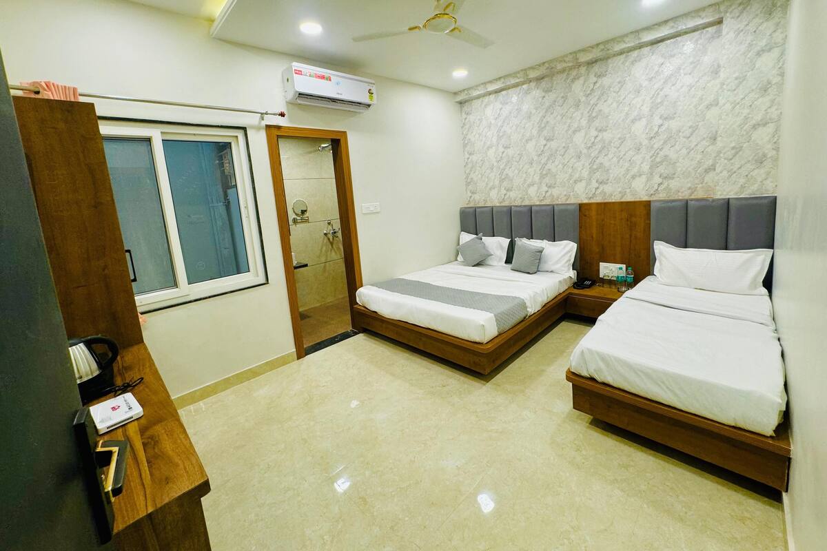 Une chambre d’hôtel avec deux lits, une armoire en bois, une salle de bain avec une porte en verre et un mur décoré d’un motif marbré.