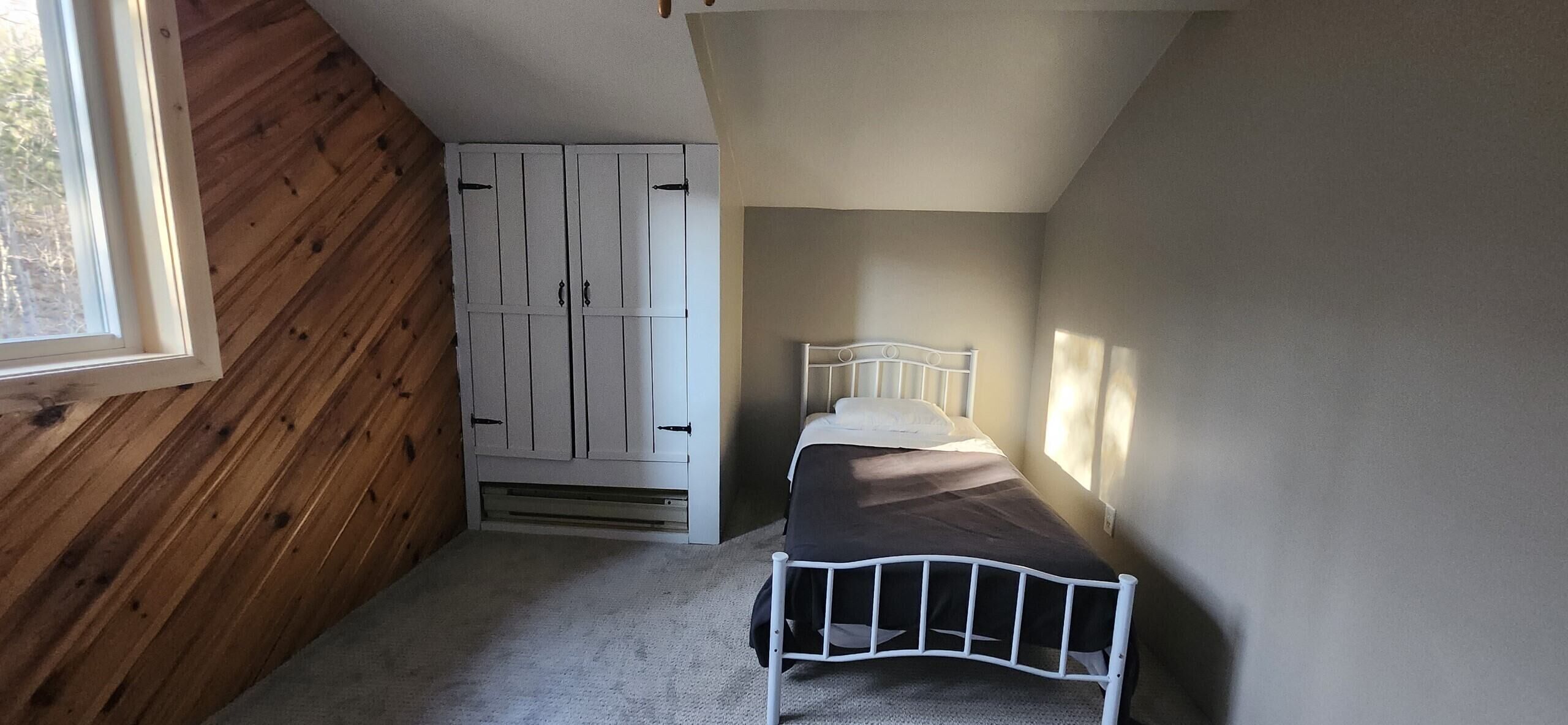 A small, narrow room with a single bed, a wardrobe, and a window.