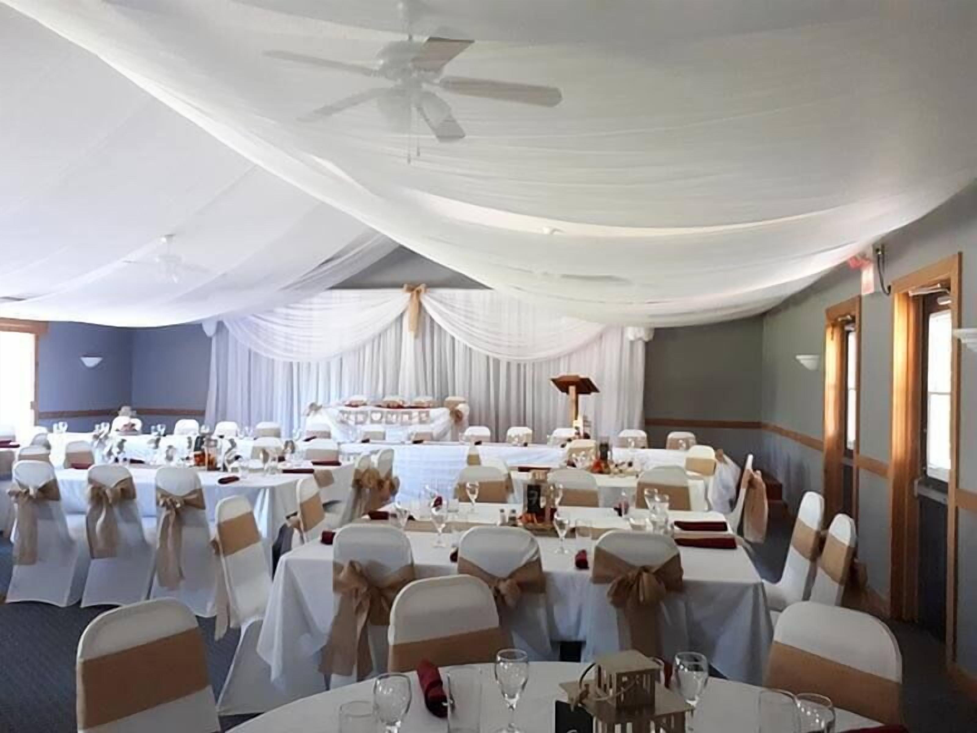 A banquet hall with round tables, white tablecloths, and chairs with beige sashes.