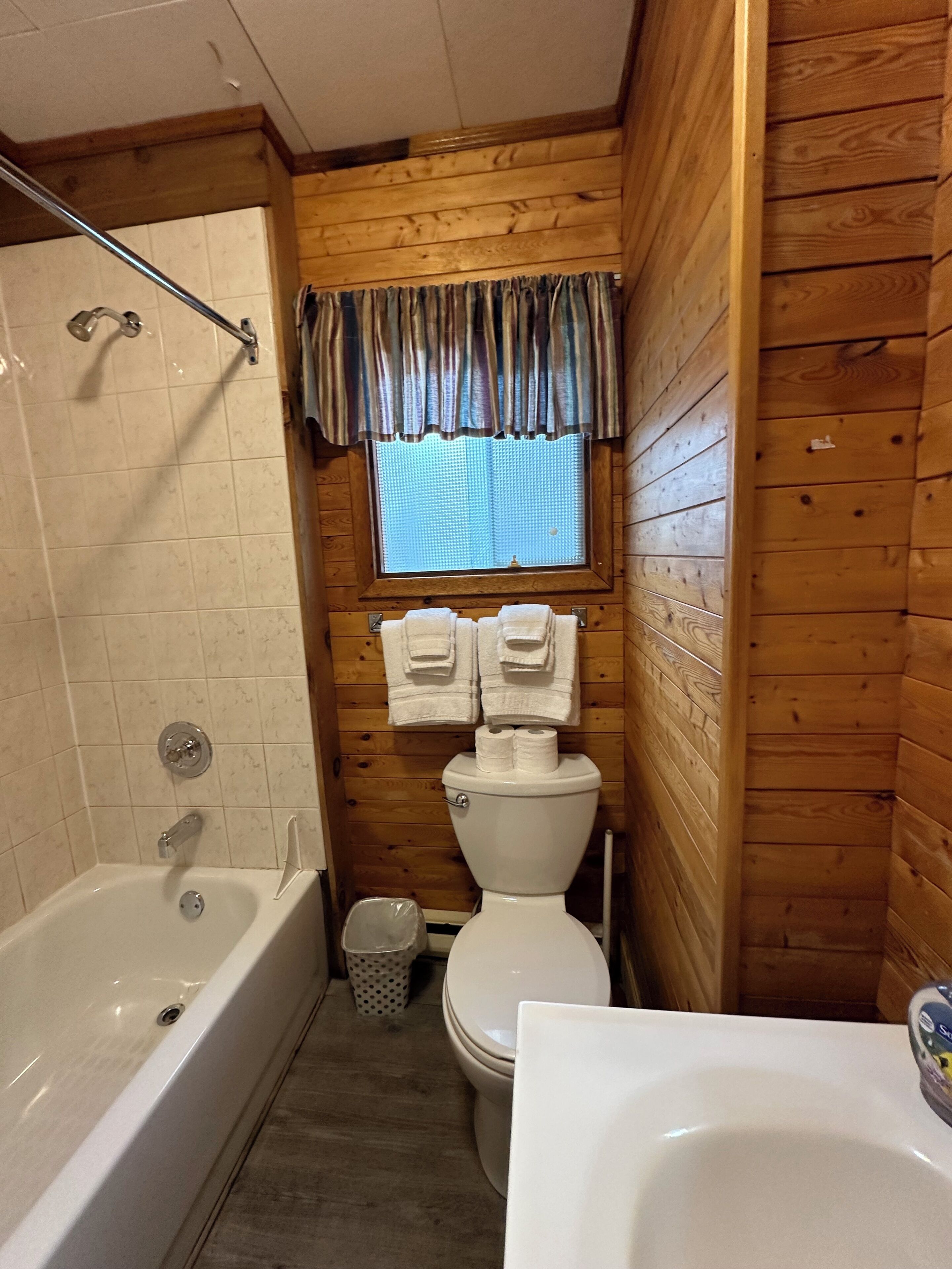 A wooden cabin bathroom with a bathtub, toilet, and sink.