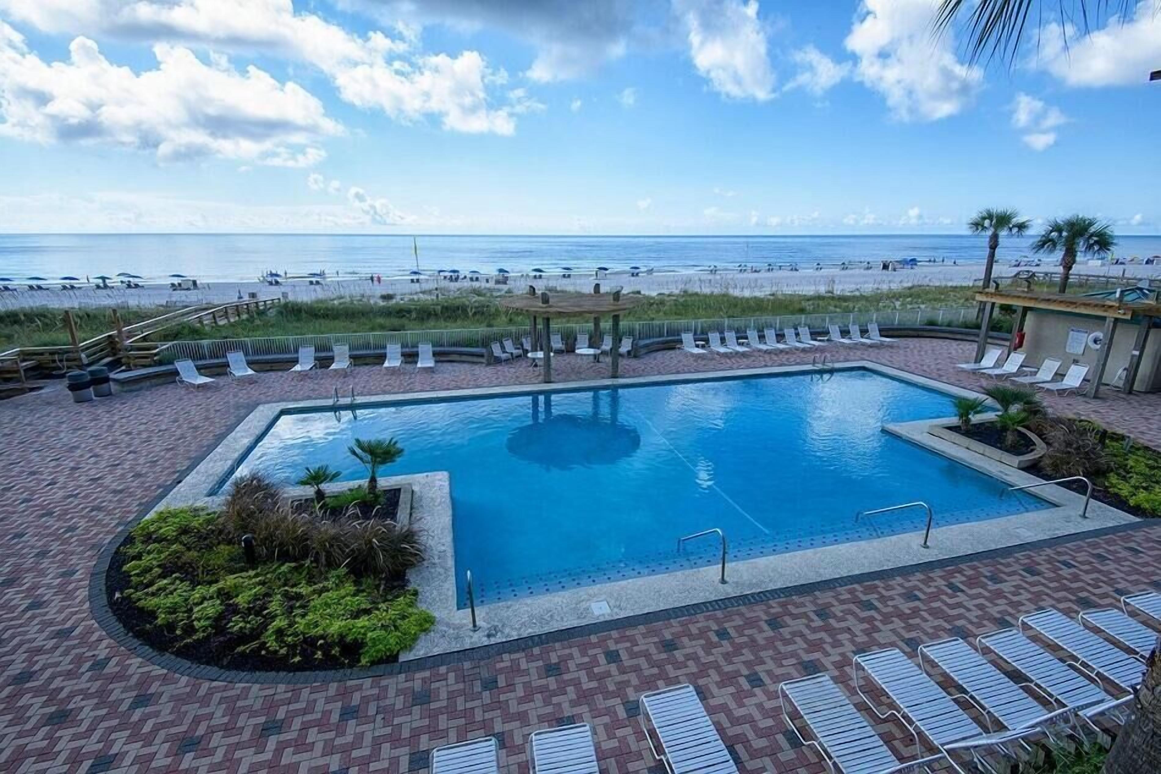 Una piscina con sillas de descanso y vista a la playa.