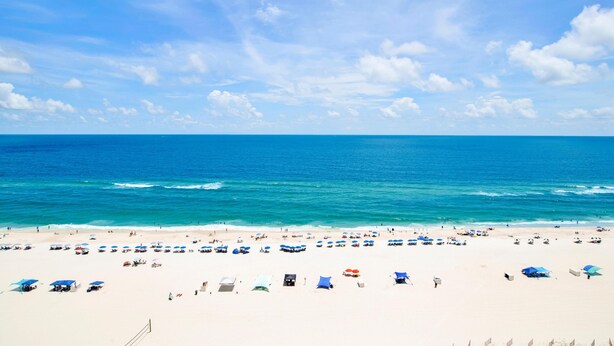 A beach with clear blue water, white sand, and numerous umbrellas. - White Caps 1502 (Orange Beach)