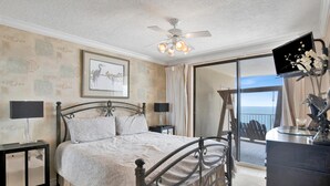 A bedroom with a bed, bedside tables, a ceiling fan, a TV, and a balcony with a view. - White Caps 1502 (Orange Beach)