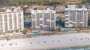 A coastal hotel complex with multiple high-rise buildings, a sandy beach, and a swimming pool. - White Caps 1502 (Orange Beach)