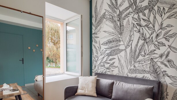 A modern living room with a grey sofa, a window with a view of a garden, and a wall with a botanical wallpaper. - La Marinière - Wifi - Bord de rivière (Laval)