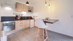 A modern kitchen with wooden cabinets, a built-in oven, a microwave, and a bar stool. - La Marinière - Wifi - Bord de rivière (Laval)