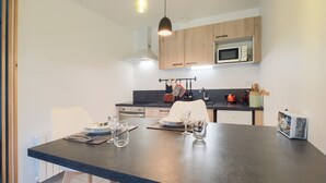 A modern kitchen with wooden cabinets, a microwave, and a dining area with a table set for two. - La Marinière - Wifi - Bord de rivière (Laval)