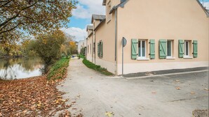 A row of beige buildings with green shutters, a paved path, and a body of water on the left. - La Marinière - Wifi - Bord de rivière (Laval)