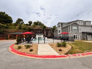 Un edificio residencial con piscina, zona de patio techada y jardín cercado.
