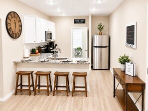 Una cocina moderna con armarios blancos, un refrigerador de acero inoxidable, un reloj y una zona con taburetes de bar.