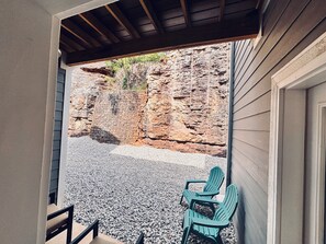 Un patio con vista a un acantilado rocoso, dos sillas verdes y una mesa de madera.