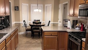 A kitchen with wooden cabinets, a central island, a dining table with chairs, a built-in oven, and a microwave.