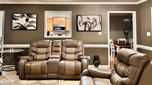 A living room with a brown leather sofa, a dining area with a table and chairs, and abstract art on the walls.