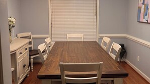 A dining room with a wooden table, white chairs, a chandelier, and a closed garage door.