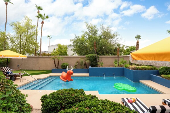 Ein Schwimmbecken mit aufblasbaren Spielzeugen, Liegestühlen und Sonnenschirmen.