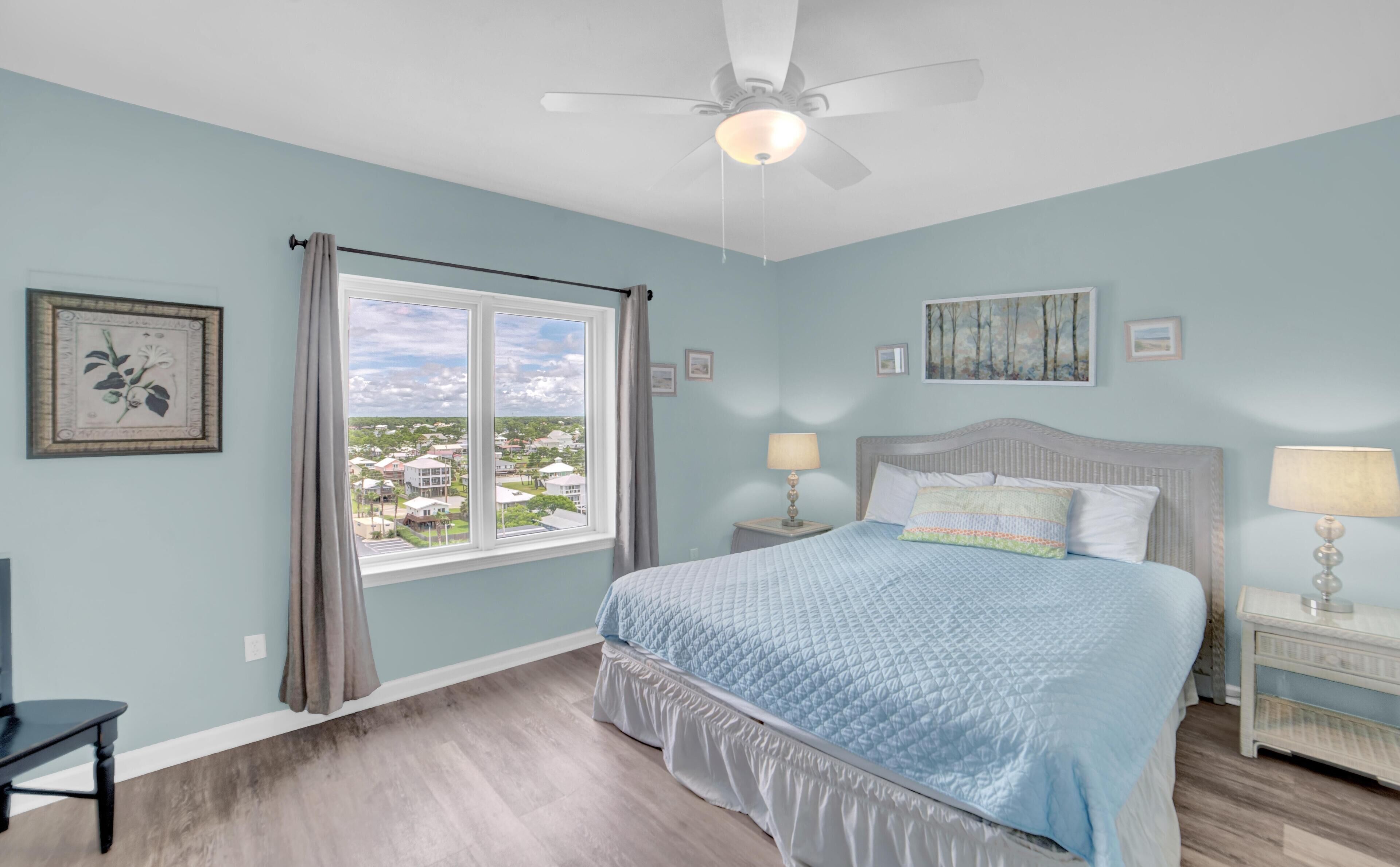 A bedroom with a bed, a nightstand, a chair, a window with curtains, and a ceiling fan.