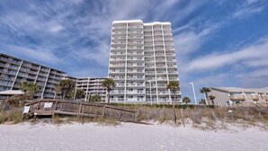 Een hoog hotel met meerdere balkons, gelegen nabij een strand met een houten promenade.