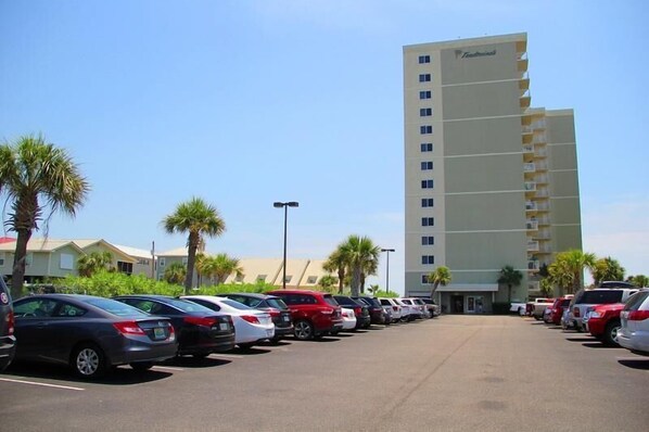 A parking lot with cars and a tall hotel building with balconies. - Tradewinds 708 (Orange Beach)