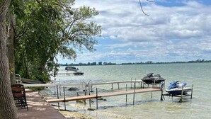 Um deck à beira do lago com um cais que se estende para a água, cercado por vegetação e um céu claro.