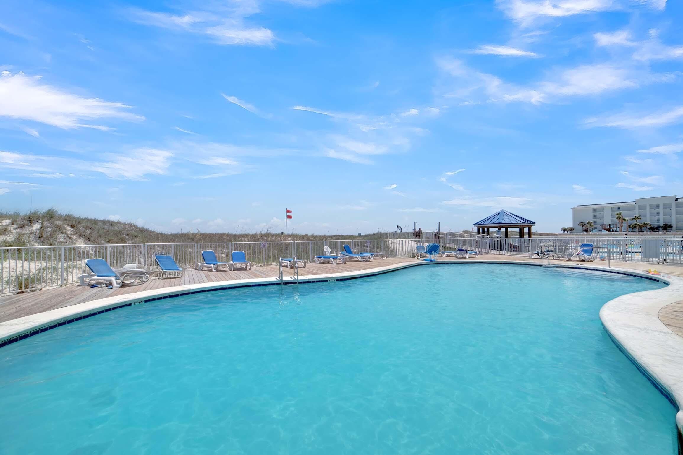 Uma piscina com cadeiras de descanso azuis e um gazebo.