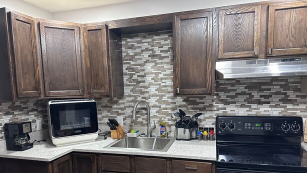 A kitchen with dark wooden cabinets, a stainless steel sink, a microwave, a stove, and a tiled backsplash. - Near Canton 3-bedroom house in  Louisville with WiFi, patio  (Louisville)
