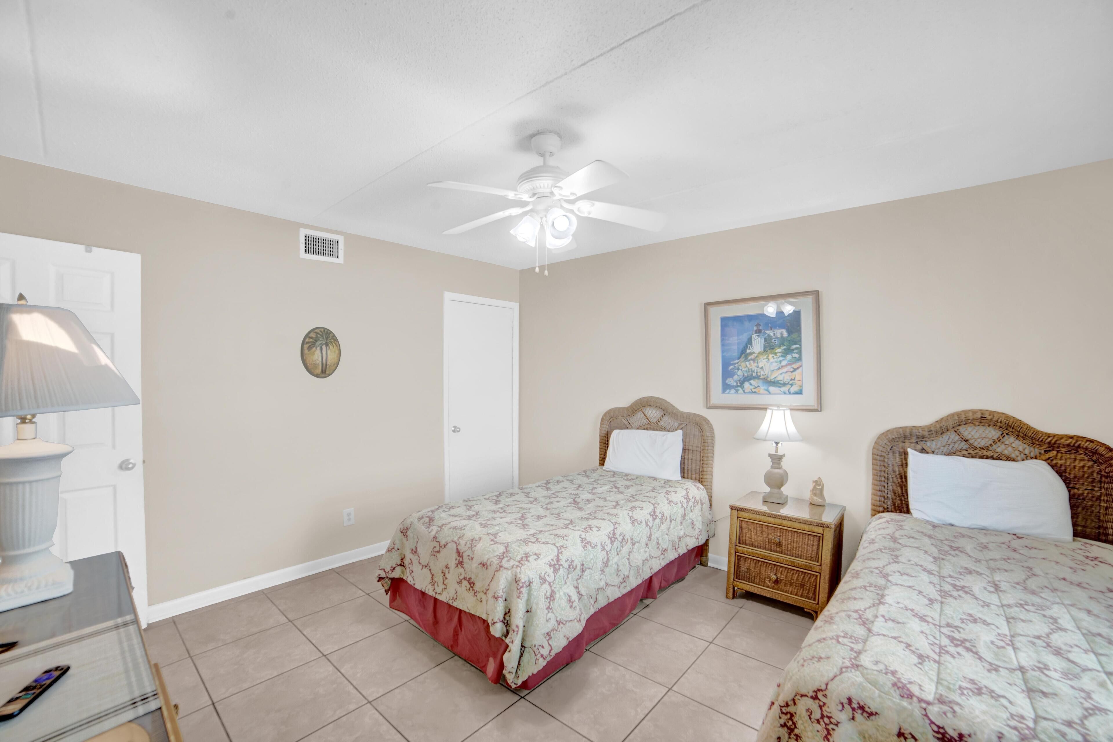 A bedroom with two beds, a ceiling fan, a nightstand with a lamp, and a framed picture on the wall.