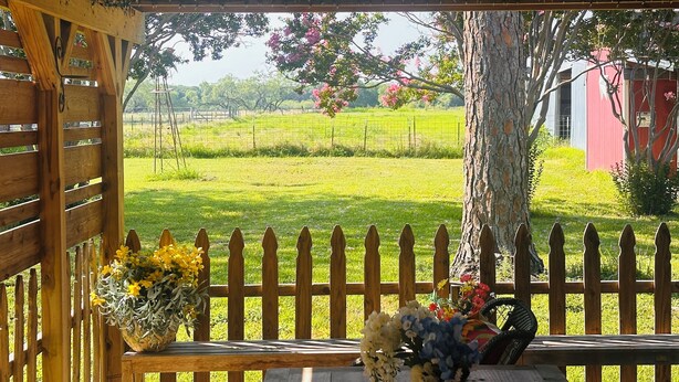 Eine Holzbalkon mit Blick auf einen umzäunten Garten und ein rotes Gebäude im Hintergrund.