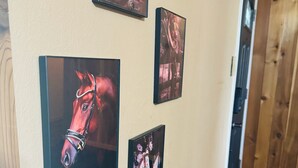 Eine Wand mit mehreren gerahmten Bildern, darunter ein auffälliges Pferdeporträt, und ein Holztisch.