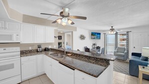 A modern kitchen with white cabinets, a granite countertop, and a ceiling fan. - Sugar Beach 230 (Orange Beach)