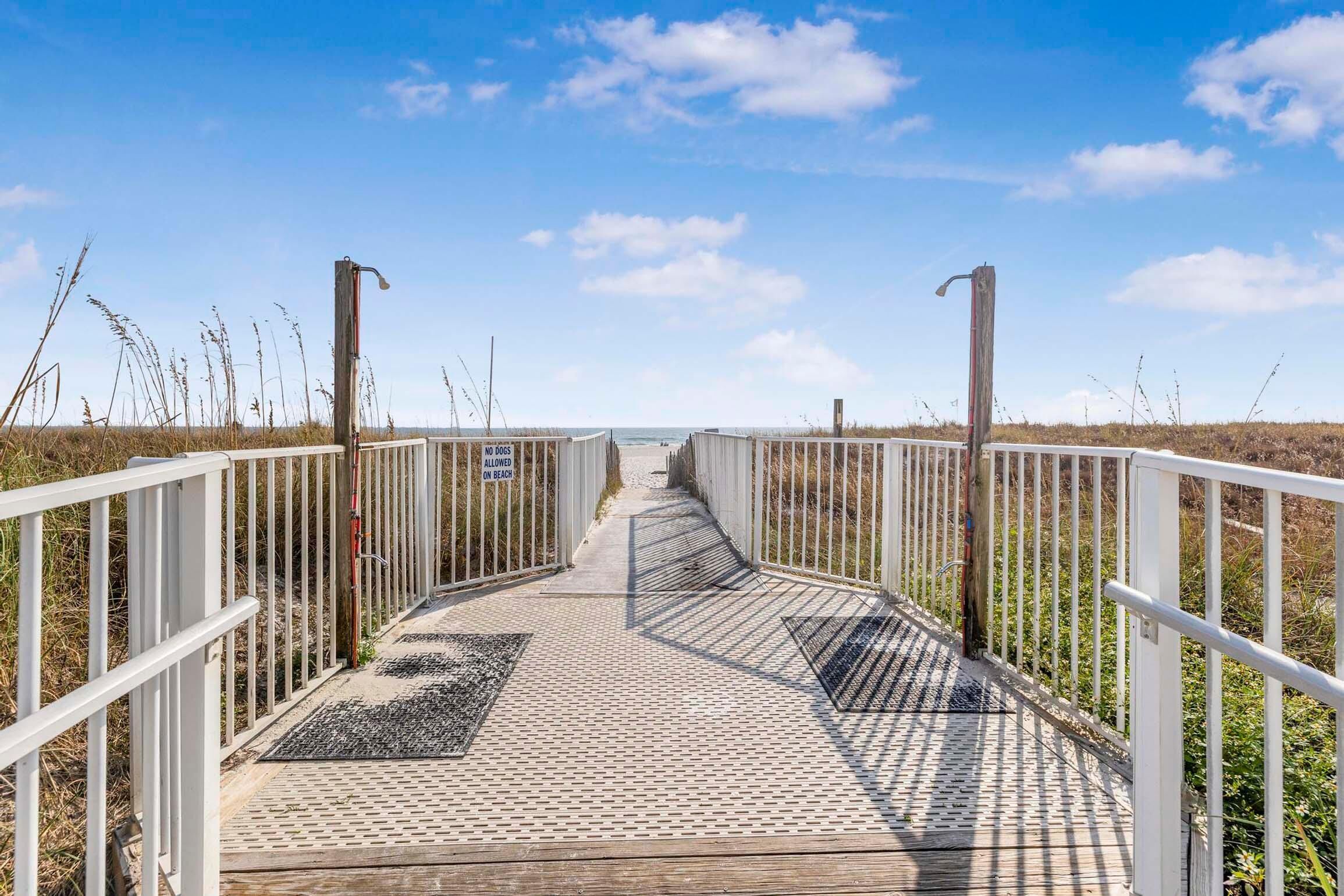 Un muelle de madera con barandillas blancas que conduce a una playa.