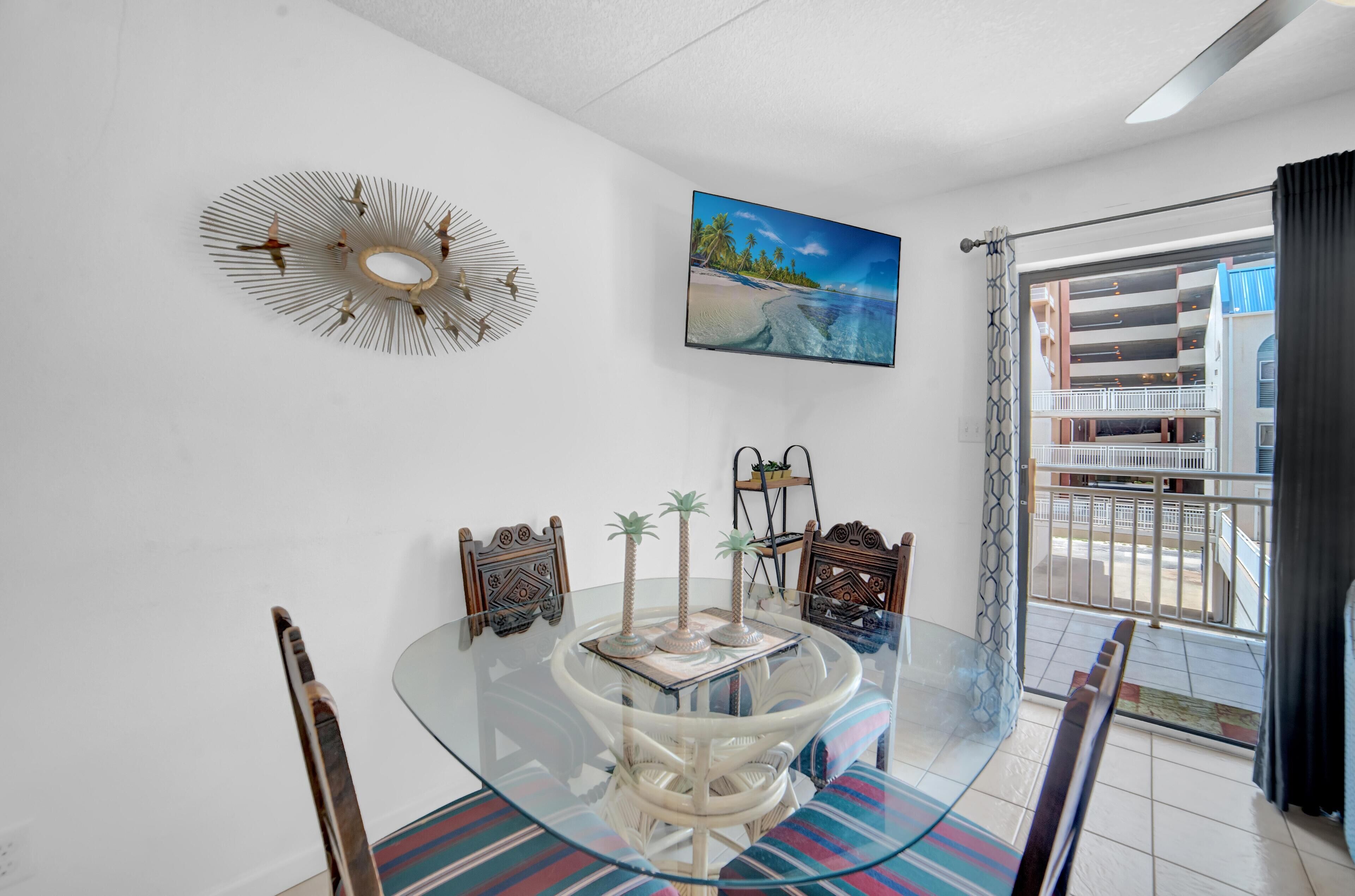 A dining area with a glass table, chairs, a decorative wall piece, and a painting of a beach scene.