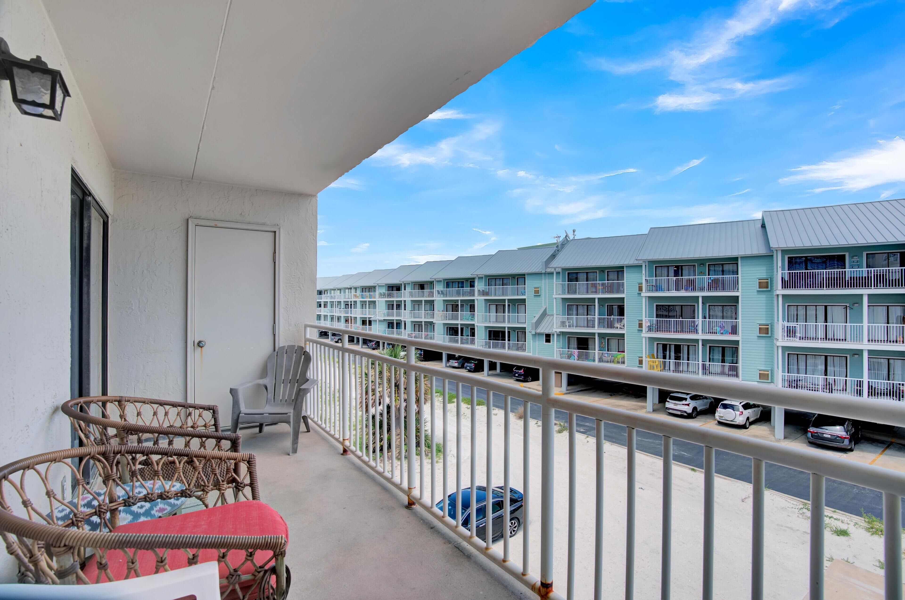 A balcony with wicker furniture and a view of a row of light blue multi-story buildings with balconies.