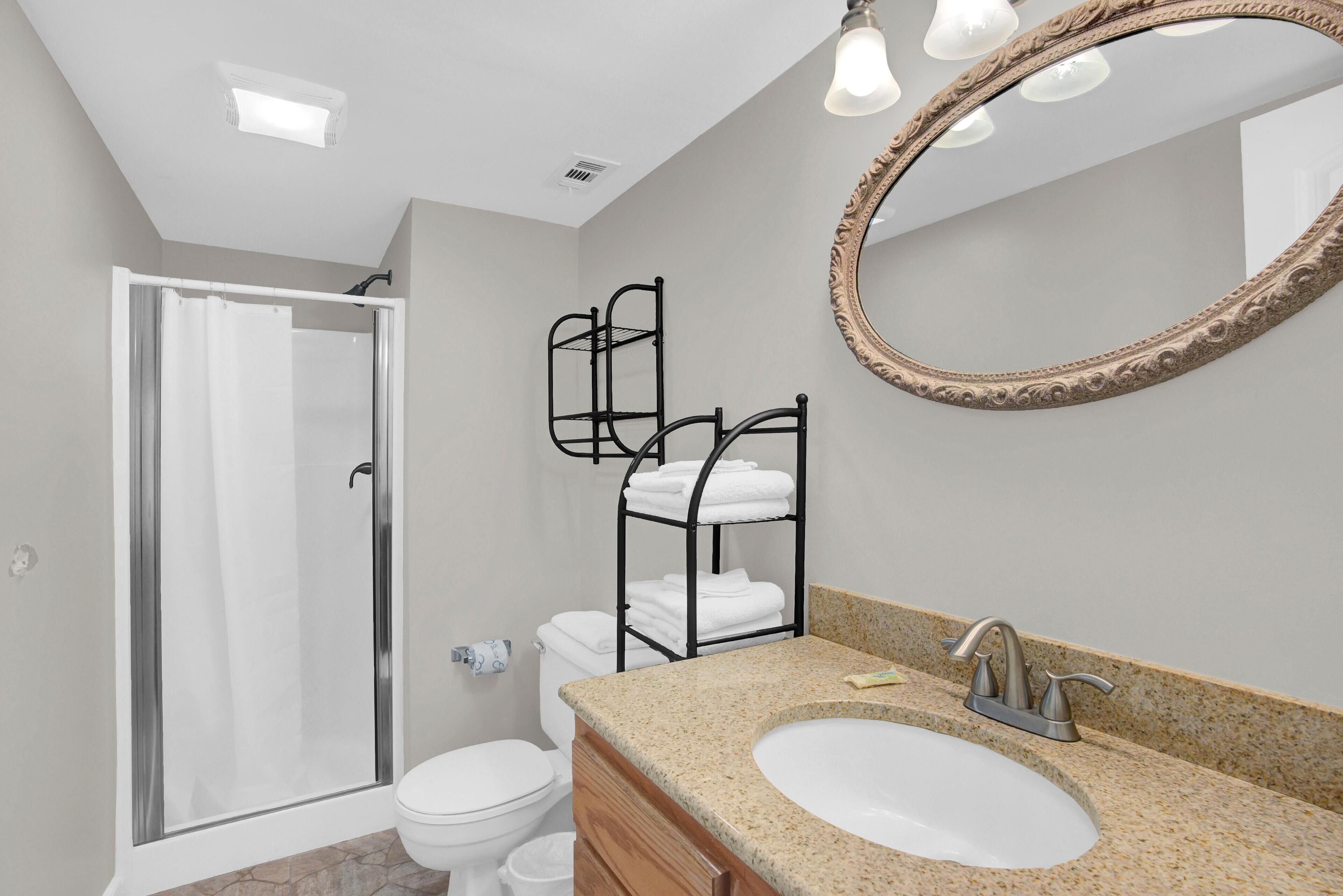 A bathroom with a shower, toilet, vanity with a sink, and a mirror.